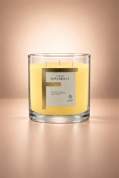 Vela aromática de Casa Fontabella en frasco Mónaco transparente con cera en tono amarillo, encendida — cera de soya y coco con tres mechas de algodón.