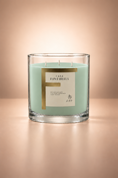 Vela aromática de Casa Fontabella en frasco Mónaco transparente con cera en tono espuma de mar, encendida — cera de soya y coco con tres mechas de algodón.