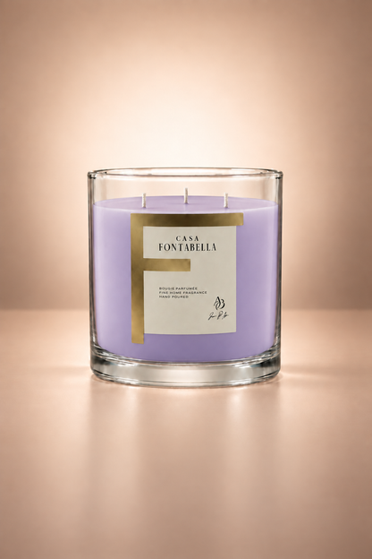 Vela aromática de Casa Fontabella en frasco Mónaco transparente con cera en tono lavanda, encendida — cera de soya y coco con tres mechas de algodón.
