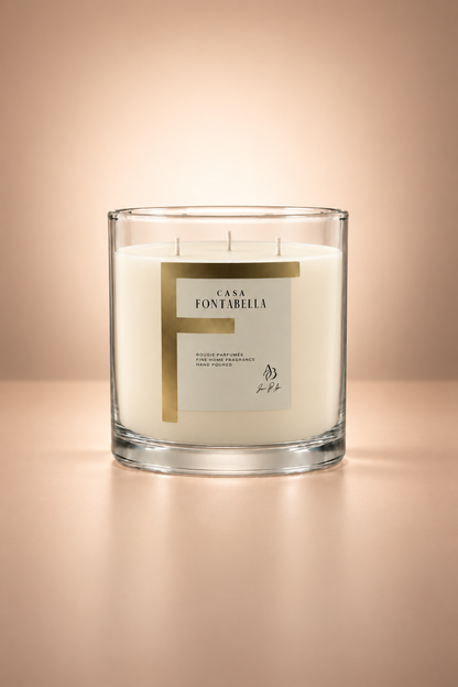 Vela aromática de Casa Fontabella en frasco Mónaco transparente con cera en su tono natural sin teñir, encendida — cera de soya y coco con tres mechas de algodón.