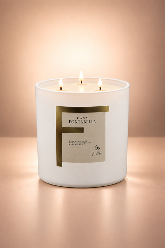 Vela aromática de Casa Fontabella en frasco Mónaco blanco mate con etiqueta dorada, encendida — cera de soya y coco con tres mechas de algodón.
