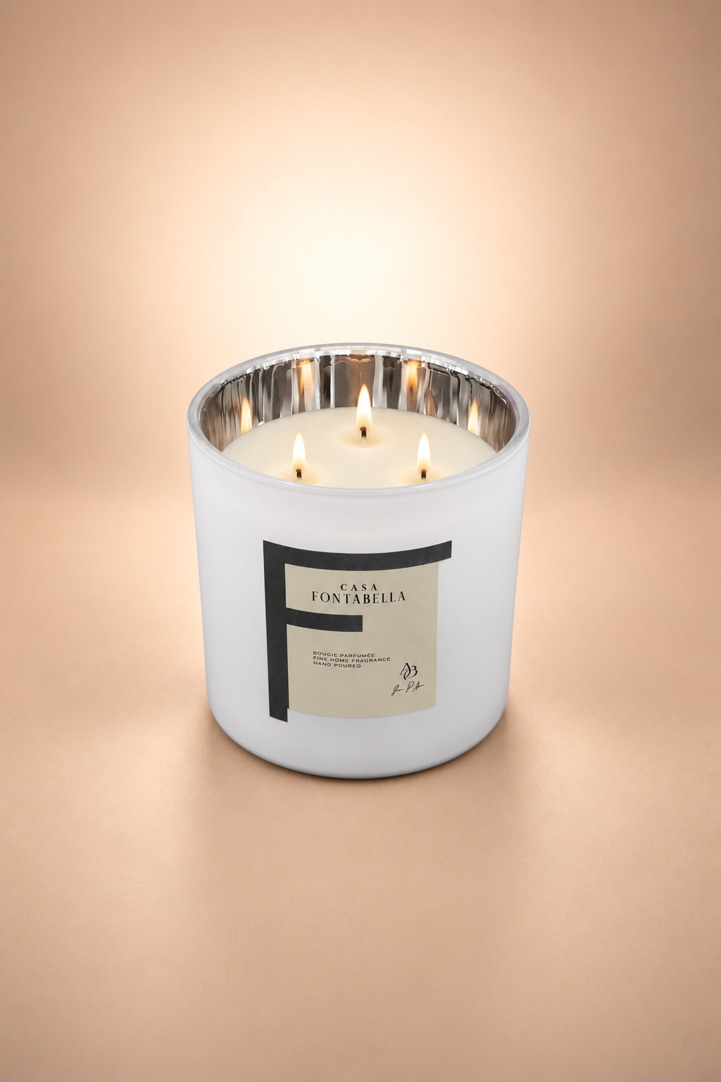 Vela aromática de Casa Fontabella en frasco Mónaco blanco mate con interior plata metálico, encendida — cera de soya y coco con tres mechas de algodón.