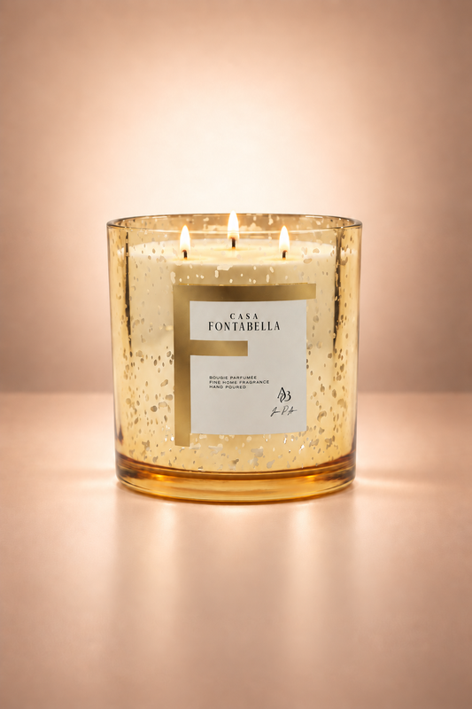 Vela aromática de Casa Fontabella en frasco Mónaco dorado con salpicaduras metálicas, encendida — cera de soya y coco con tres mechas de algodón.